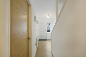 A hallway with a wooden door, a white wall, a radiator, and a light fixture.