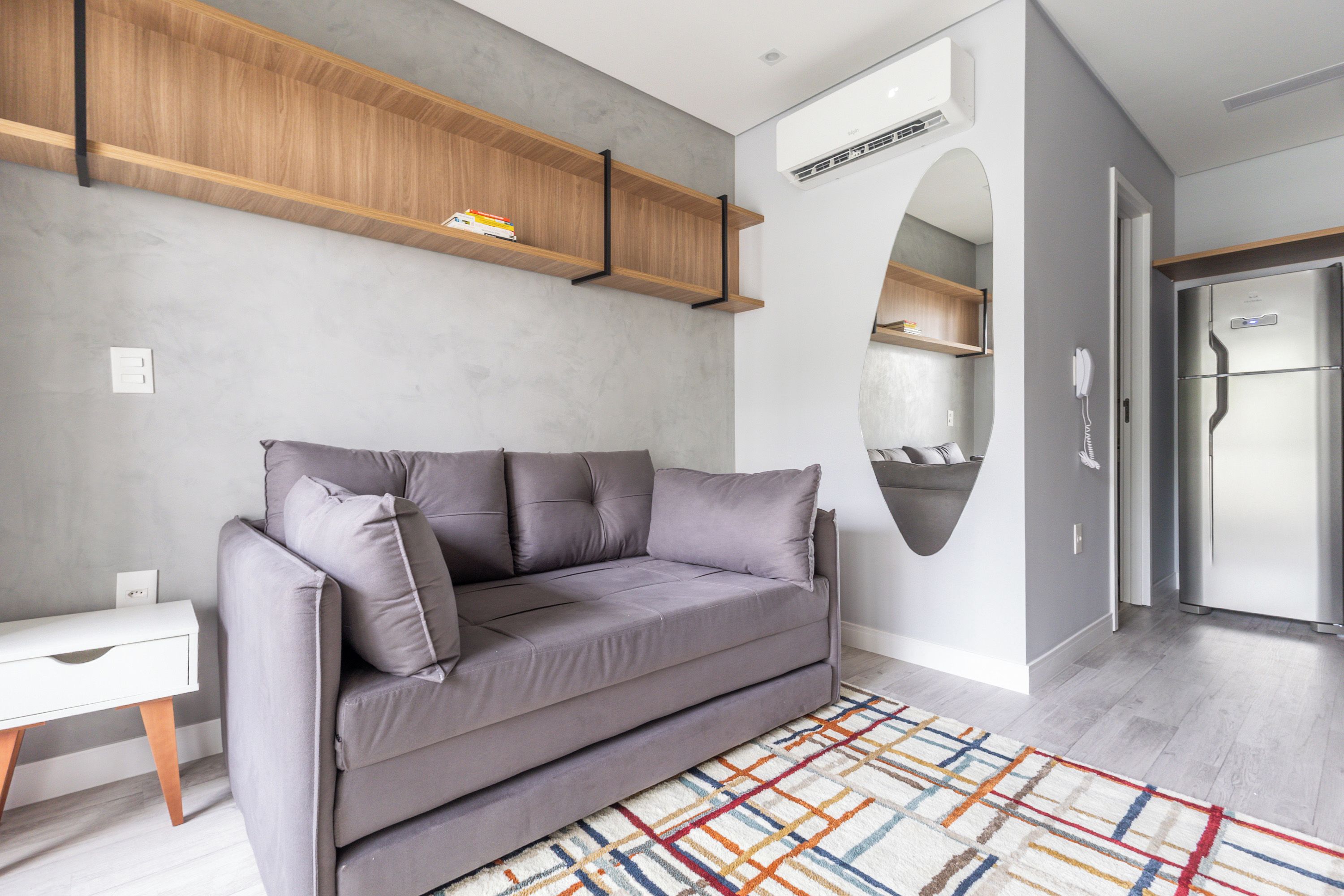 A modern living room with a grey sofa, a white side table, a patterned rug, and built-in wooden shelves.