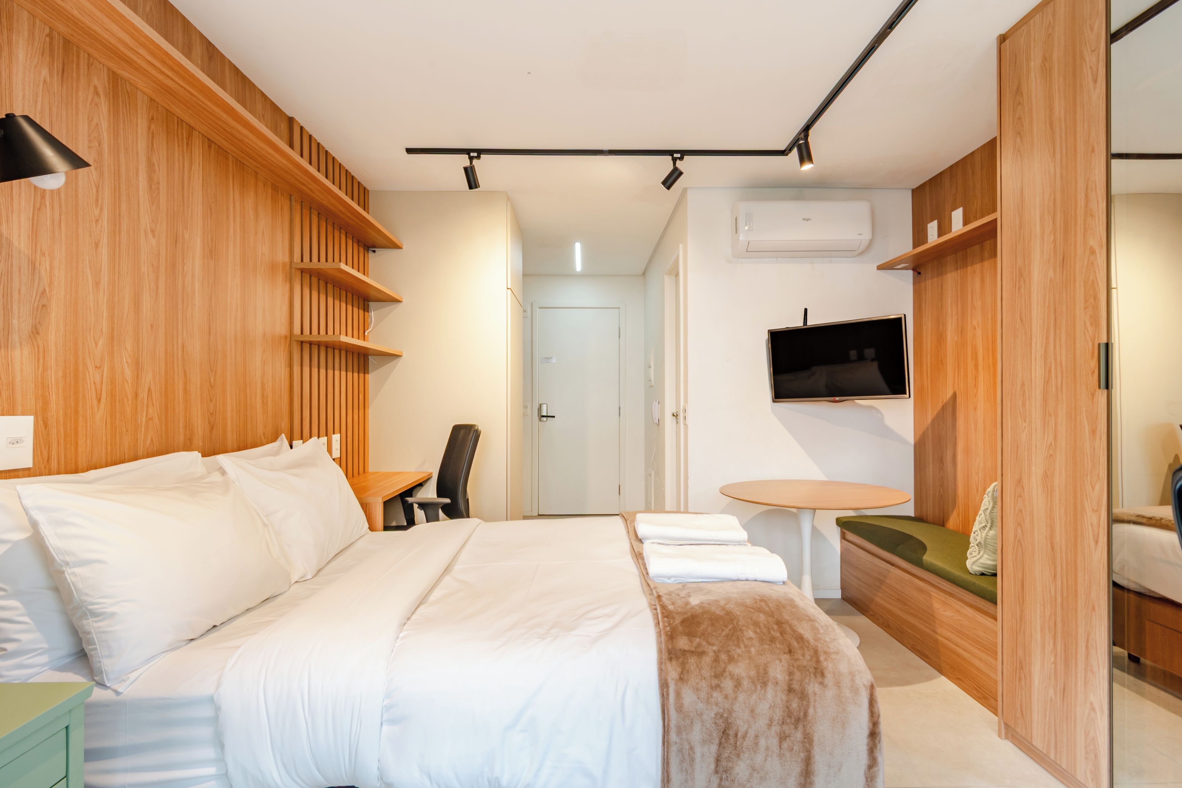 Une chambre d’hôtel moderne équipée d’un grand lit, d’un bureau, d’une chaise, d’une petite table et d’un téléviseur fixé au mur.