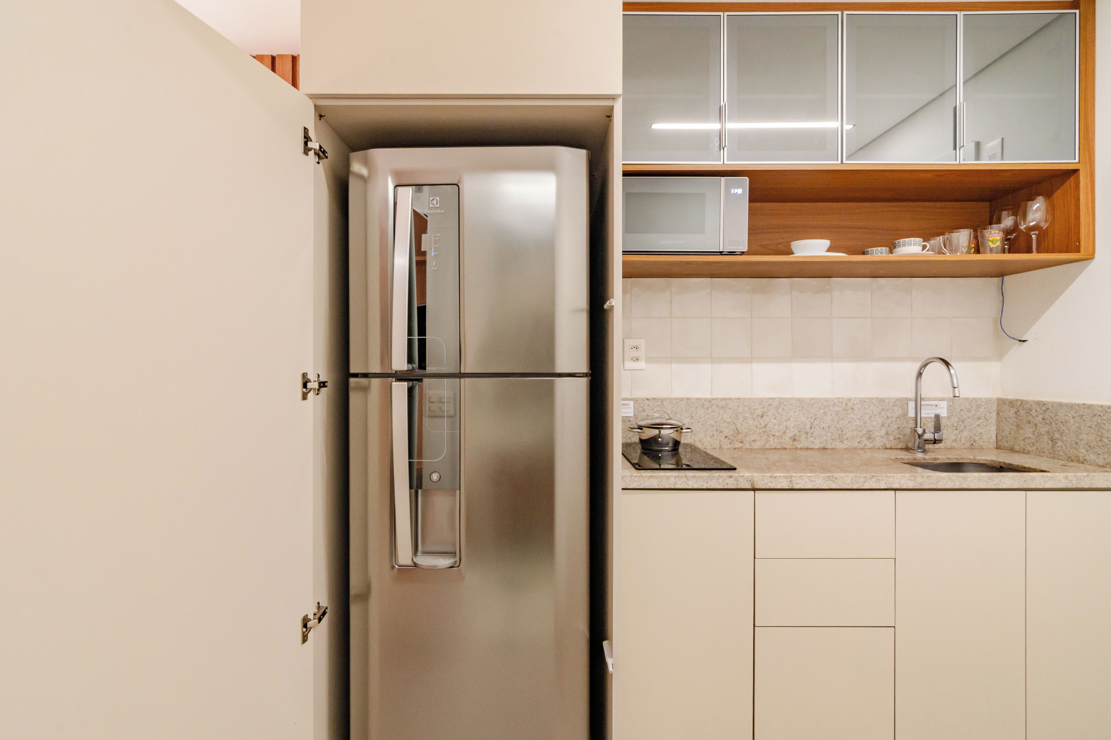 A kitchen with a stainless steel refrigerator, a sink, and wooden cabinets.