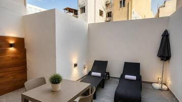 A modern outdoor patio with a dining table, two lounge chairs, and a potted plant.