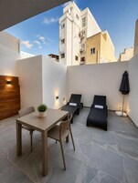 A modern outdoor patio with a dining table, two lounge chairs, and a potted plant.