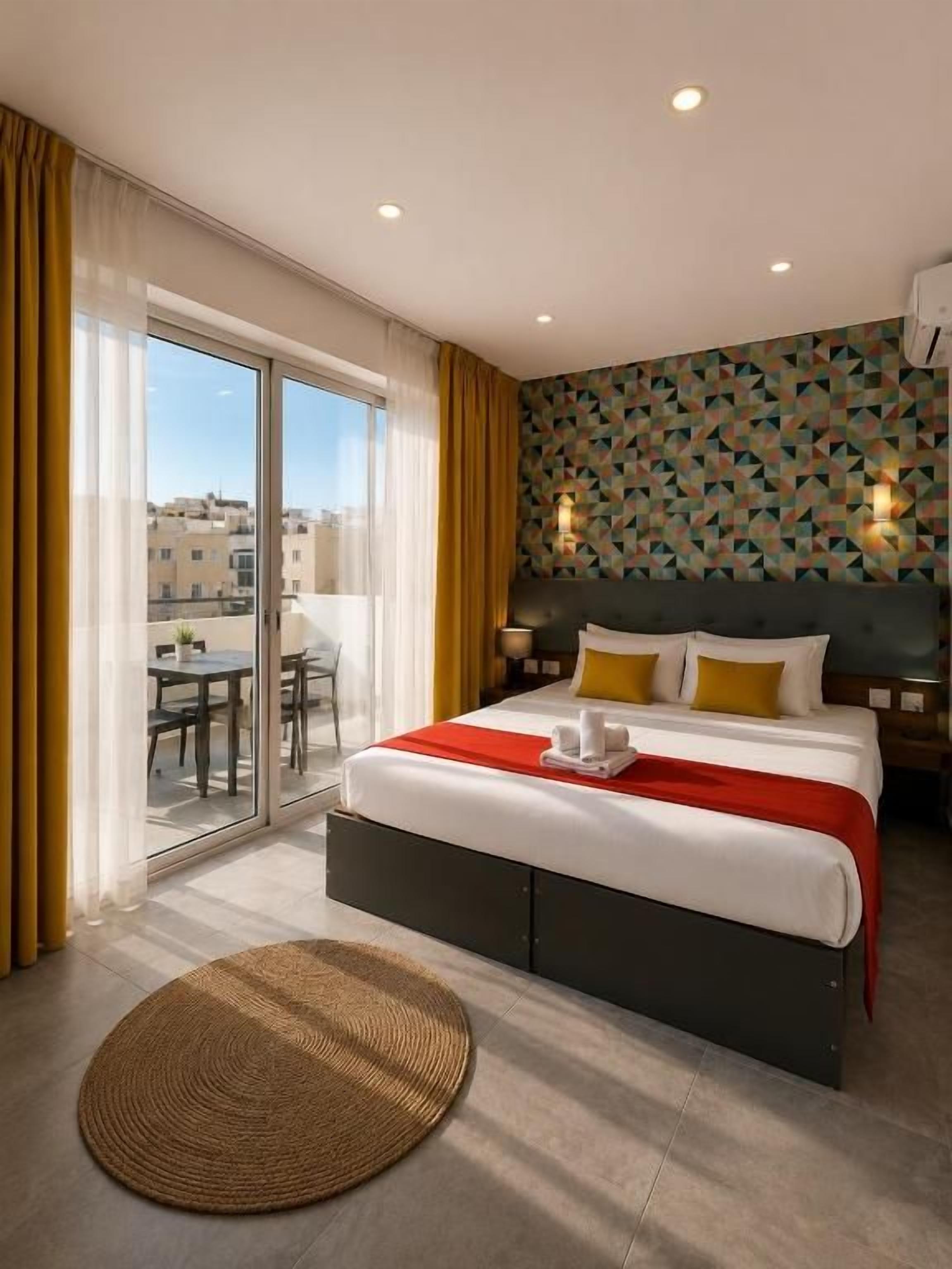 Quarto de hotel com uma cama grande, vista por uma porta deslizante para área externa e parede com padrão.