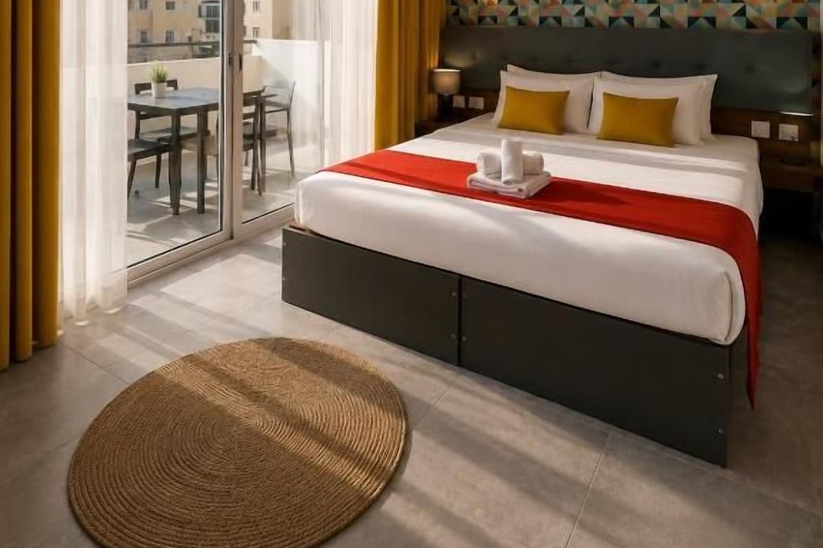 Quarto de hotel com uma cama grande, vista por uma porta deslizante para área externa e parede com padrão.