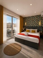 A hotel room with a large bed, a view through a sliding door to an outdoor area, and a patterned wall.