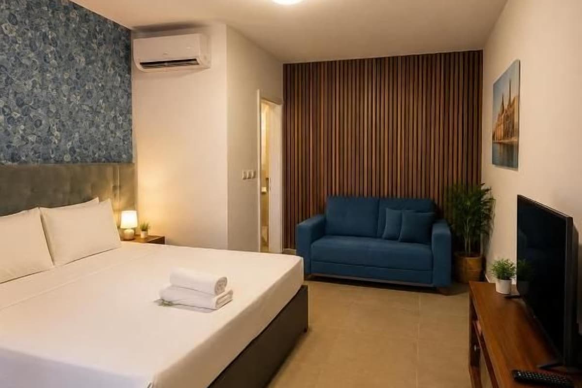 Quarto de hotel com cama, sofá, televisão e ar condicionado fixado na parede.