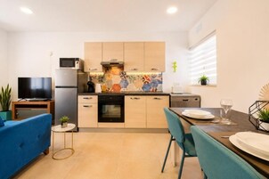 Cocina compacta con electrodomésticos modernos, zona de comedor con mesa y sillas, y un televisor sobre un mueble.