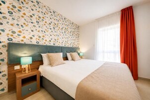 Una habitación de hotel con una cama, mesitas de noche, cabecera y una ventana con cortinas.