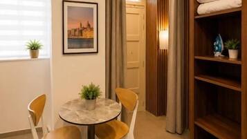 Una habitación con una mesa redonda, cuatro sillas, una planta en maceta, un cuadro enmarco, una estantería de madera y una puerta que da a otra habitación.