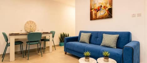 A living room with a blue sofa, two small round tables, and a dining area with chairs and a table.