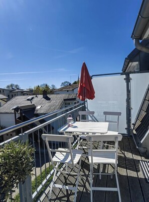 Eine Dachterrasse mit Tisch und Stühlen, einem roten Sonnenschirm und Blick auf benachbarte Gebäude.