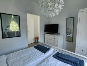 Ein Schlafzimmer mit zwei Betten, einem Fernseher, einem Spiegel und einer weißen Deckenleuchte.