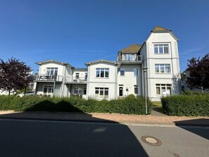 Ein mehrstöckiges Wohngebäude mit flachem Dach, Balkonen und blauem Himmel.