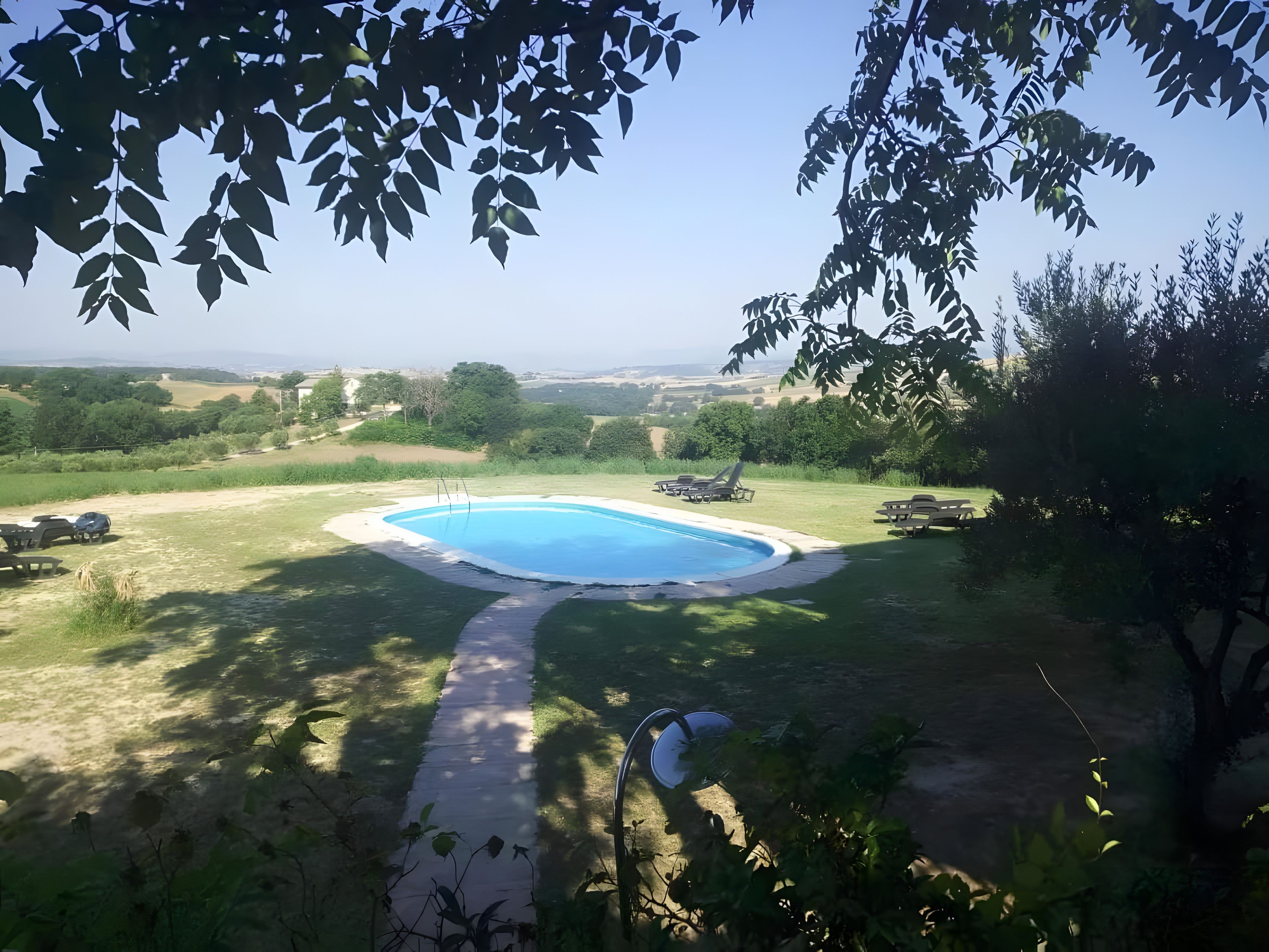 A swimming pool with a surrounding deck, a clear sky, and a view of distant fields.