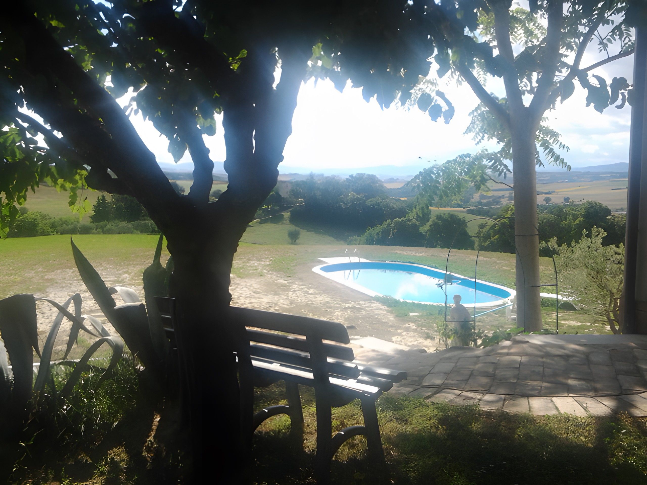 Uma área de pátio com banco, piscina e vista para o campo.