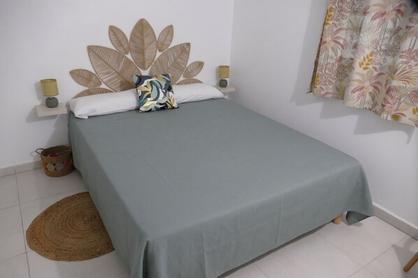A bed with a grey bedspread, a decorative pillow, two wall-mounted lamps, and a woven rug on the floor. - Les Gîtes d'Anna Blue " Côté Nature (Sainte-Anne)