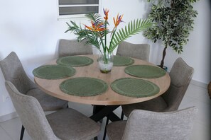 A round wooden table with six chairs, each with a green placemat. A vase with flowers is placed in the center. - Les Gîtes d'Anna Blue " Côté Nature (Sainte-Anne)