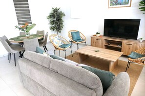 A modern living room with a sofa, two chairs, a coffee table, a television, and a small plant. - Les Gîtes d'Anna Blue " Côté Nature (Sainte-Anne)