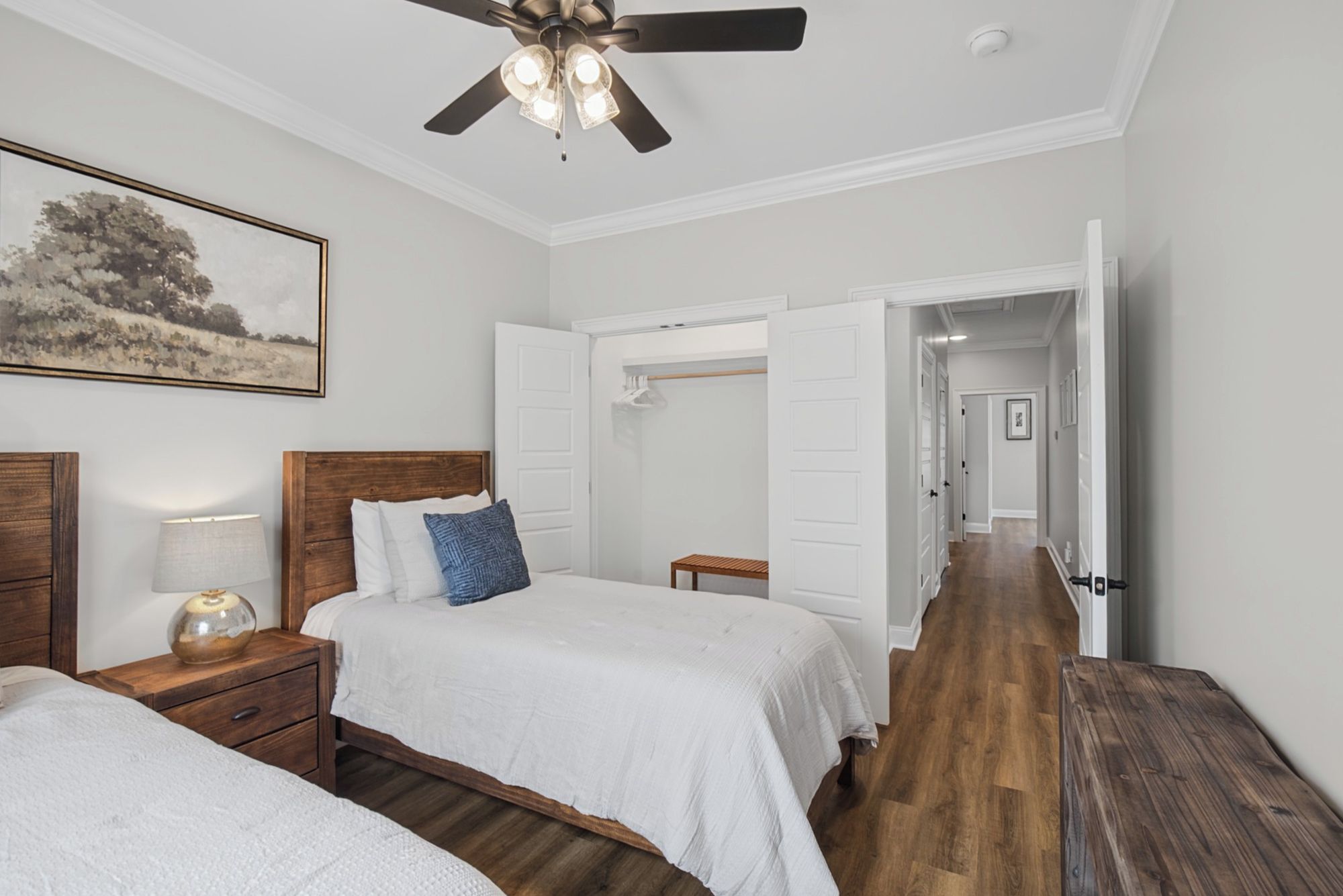 A bedroom with two beds, a ceiling fan, a nightstand with a lamp, and a painting on the wall.