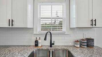 A kitchen with white cabinets, a double sink, a window with blinds, and decorative containers on the countertop.