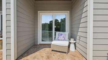 A covered porch with a wicker chair and a small table, a sliding glass door leading to a backyard, and a white exterior wall.