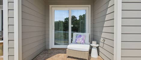 A covered porch with a wicker chair and a small table, a sliding glass door leading to a backyard, and a white exterior wall.