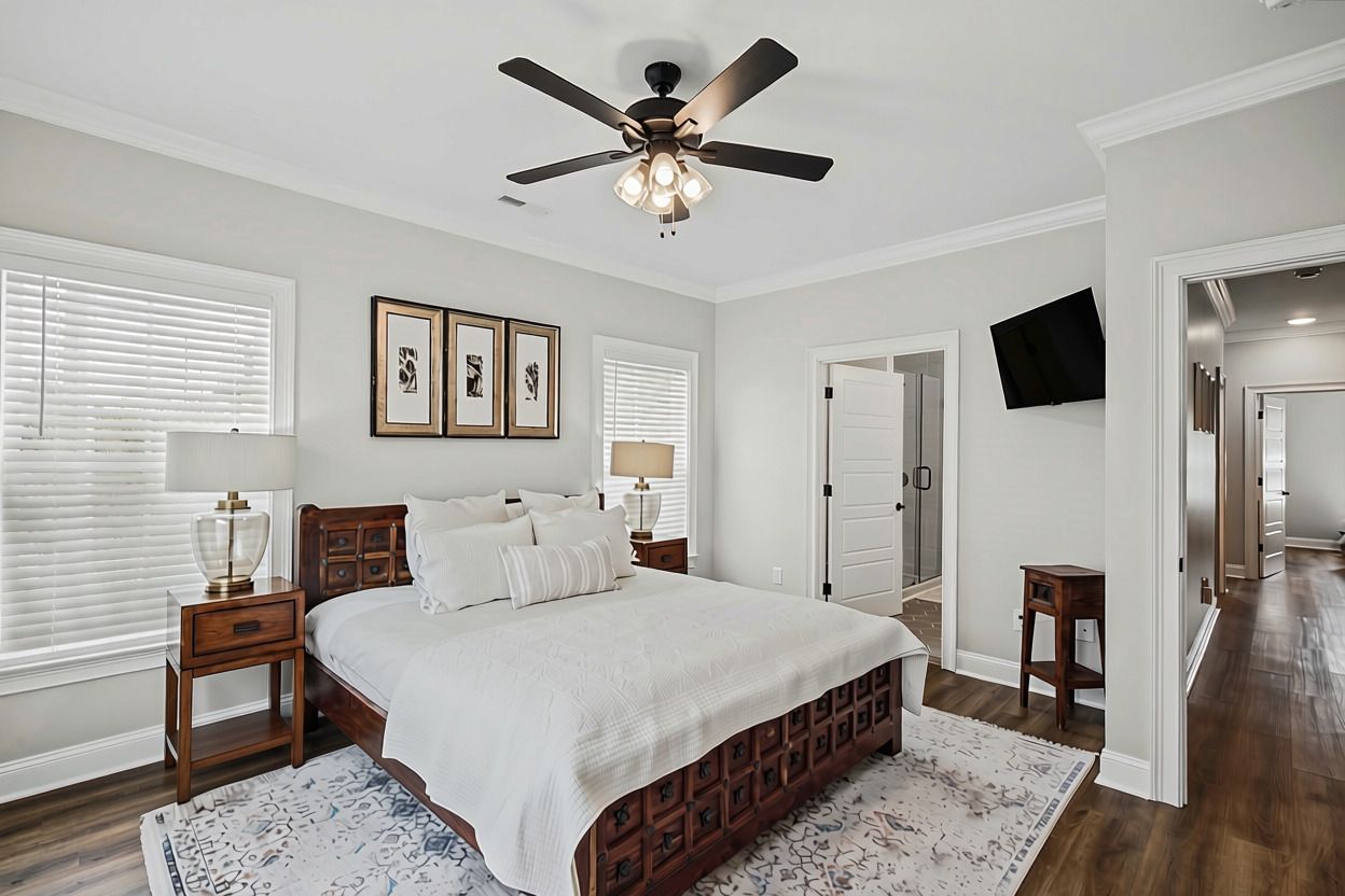 Une chambre à coucher comprenant un lit, des tables de chevet, un ventilateur de plafond, des tableaux encadrés accrochés au mur et un téléviseur fixé au mur.