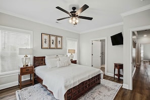 Une chambre à coucher comprenant un lit, des tables de chevet, un ventilateur de plafond, des tableaux encadrés accrochés au mur et un téléviseur fixé au mur.