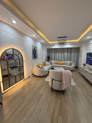 A modern living room with a sectional sofa, a round coffee table, and a TV. - 2-bedroom with Extra Room in Nairobi,Westlands Near Sarit, with pool, gym, cafes (Nairobi)