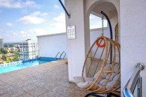 A balcony with a hanging chair, a pool, and a view of buildings. - 2-bedroom with Extra Room in Nairobi,Westlands Near Sarit, with pool, gym, cafes (Nairobi)
