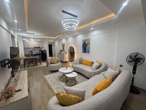 A modern living room with a sofa, coffee table, and a dining area with chairs. - 2-bedroom with Extra Room in Nairobi,Westlands Near Sarit, with pool, gym, cafes (Nairobi)