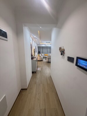 A hallway leading to a living area with a sofa, a coffee table, and a flat-screen TV mounted on the wall. - 2-bedroom with Extra Room in Nairobi,Westlands Near Sarit, with pool, gym, cafes (Nairobi)