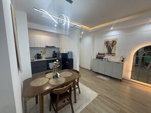 A modern kitchen with white cabinets, a dining area with a wooden table and chairs, and a kitchen island with a water dispenser. - 2-bedroom with Extra Room in Nairobi,Westlands Near Sarit, with pool, gym, cafes (Nairobi)