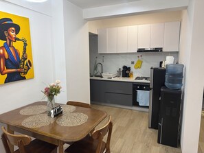A modern kitchen with white cabinets, a black refrigerator, and a dining table with a placemat. - 2-bedroom with Extra Room in Nairobi,Westlands Near Sarit, with pool, gym, cafes (Nairobi)