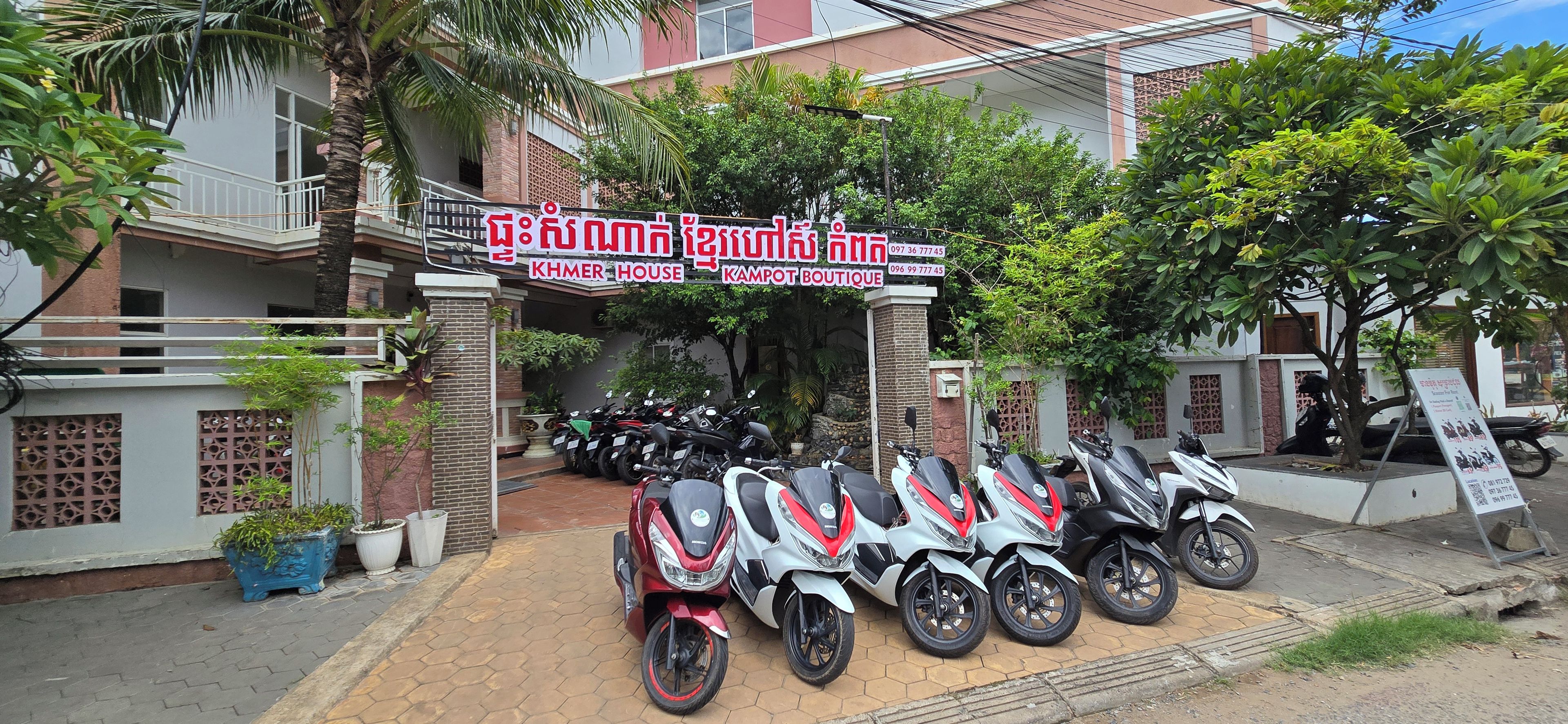 A building with a signboard, a row of motorcycles parked in front, and a gated entrance.