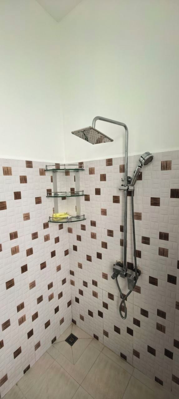Une salle de bain avec une douche, des murs carrelés et une étagère d’angle.