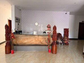 Zona de recepción con un mostrador de madera, pared con diseño y estatuas tradicionales.