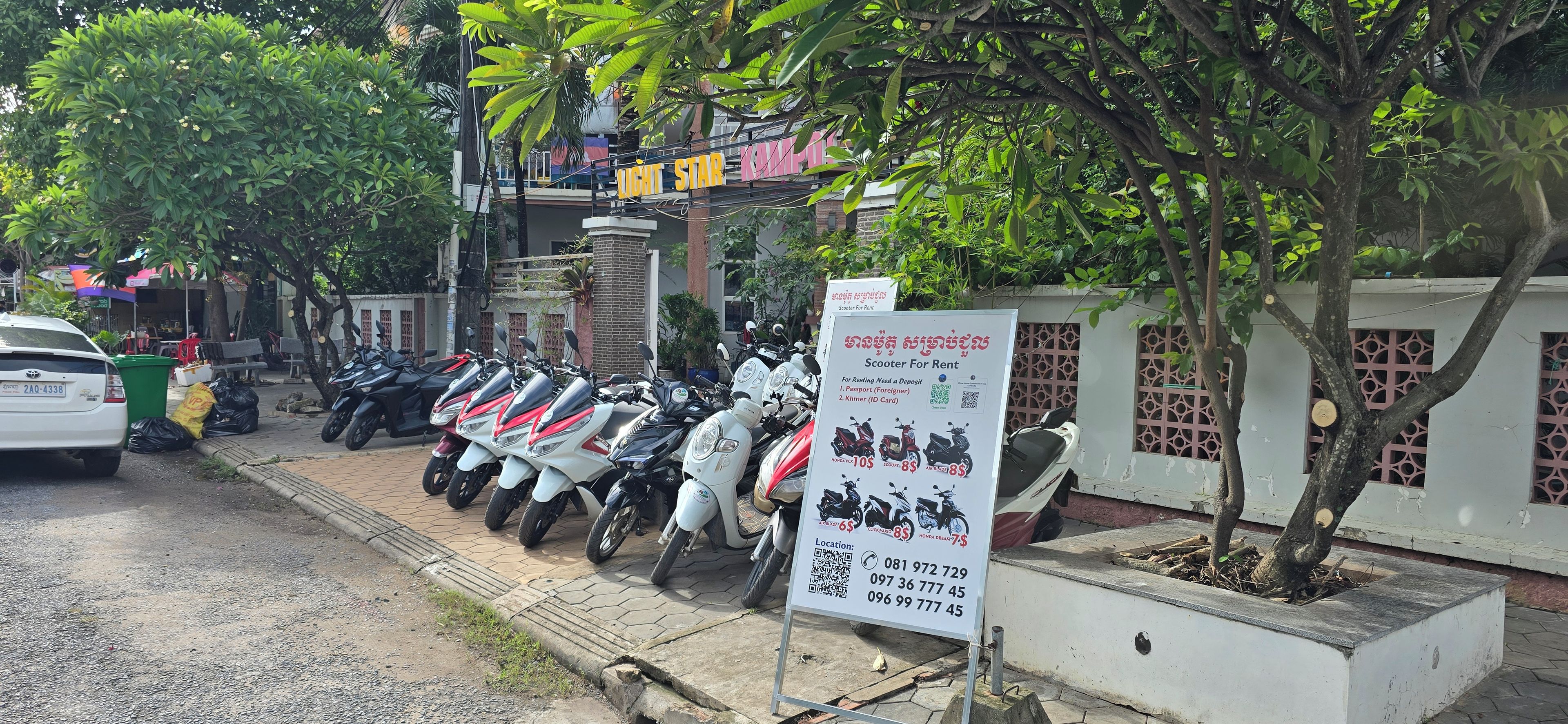 A row of scooters parked in front of a building with a signboard advertising scooter rentals.