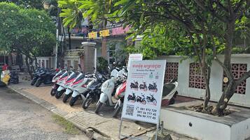 A row of scooters parked in front of a building with a signboard advertising scooter rentals.