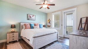 Une chambre à coucher avec un lit, des tables de chevet, un ventilateur de plafond, une fenêtre et une porte.