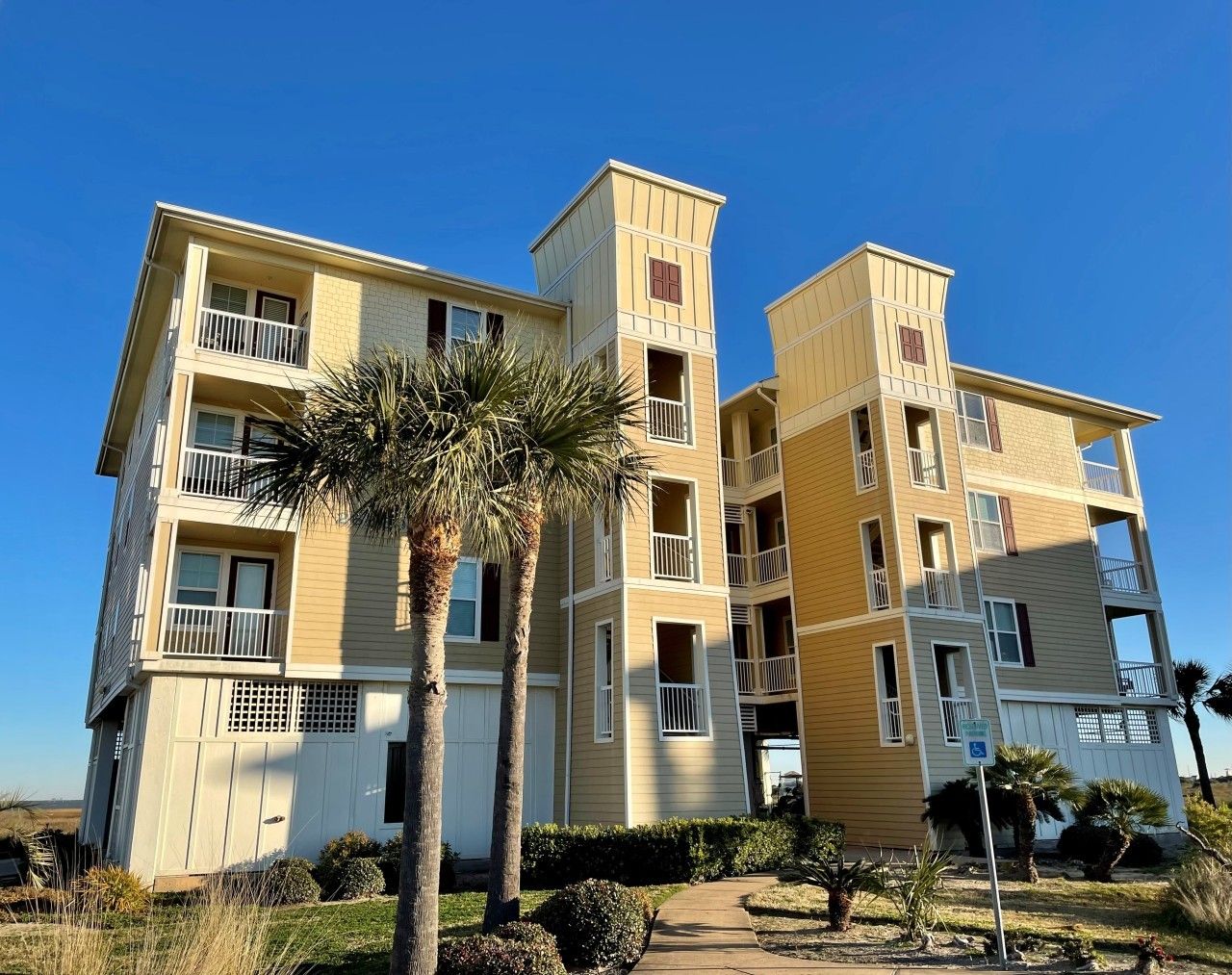 A multi-story residential building with balconies, a clear sky, and a palm tree in the foreground.