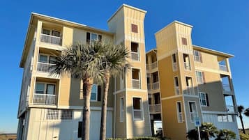 A multi-story residential building with balconies, a clear sky, and a palm tree in the foreground.