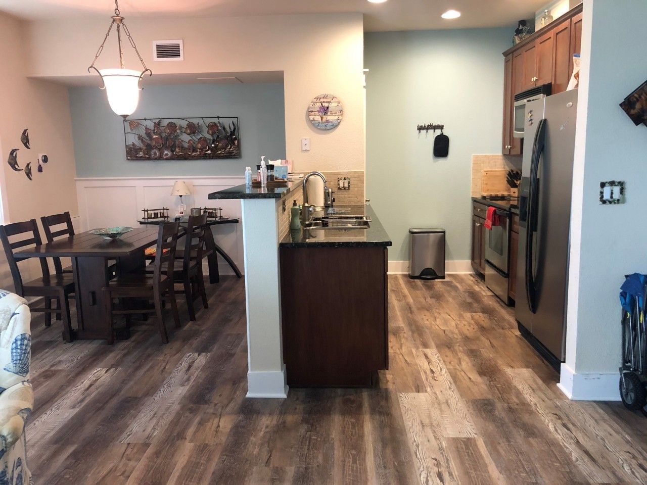 A kitchen with a dining area, wooden flooring, a refrigerator, and a clock on the wall.