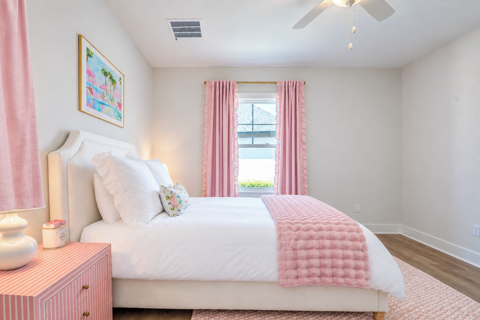 Quarto com cama, mesa de cabeceira, ventoinha no teto e janela com cortinas.