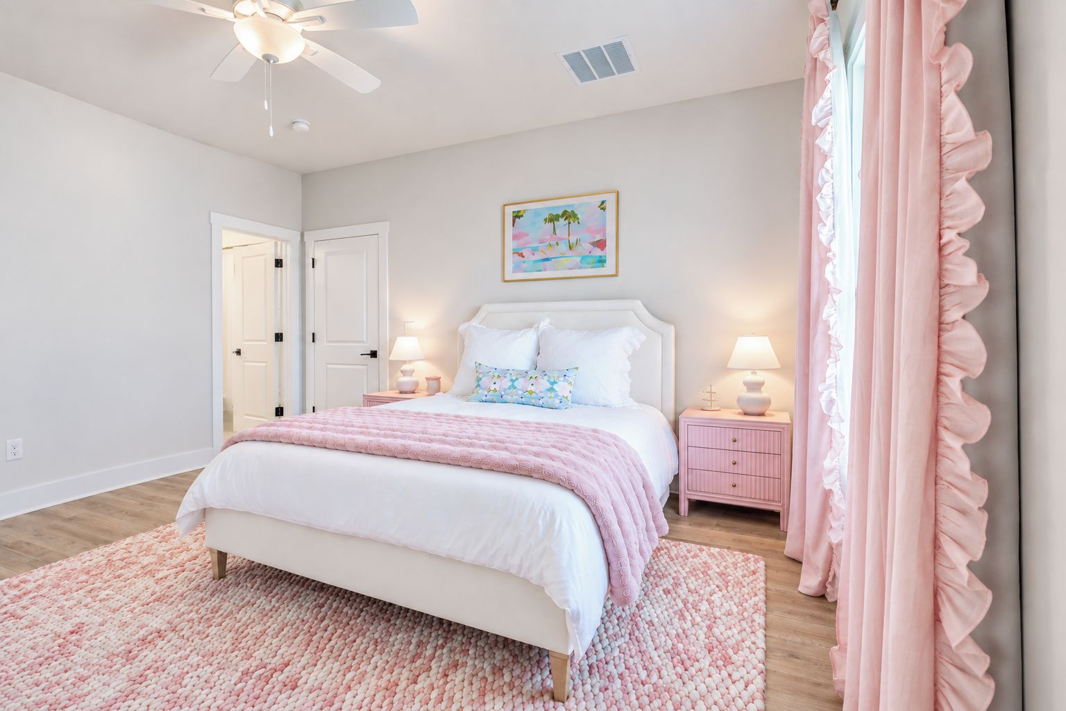 A bedroom with a bed, bedside tables, a ceiling fan, a door, and a wall-mounted painting.