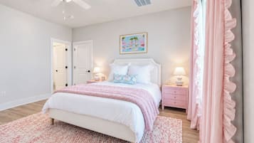 A bedroom with a bed, bedside tables, a ceiling fan, a door, and a wall-mounted painting.