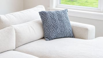 A white sofa with a patterned pillow in front of a window with a view of a green field.