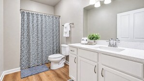 A bathroom with a shower curtain, toilet, sink, and cabinets. - The Rebel Landing, Pool+3BR by Velvet Ditch Villas (Oxford)