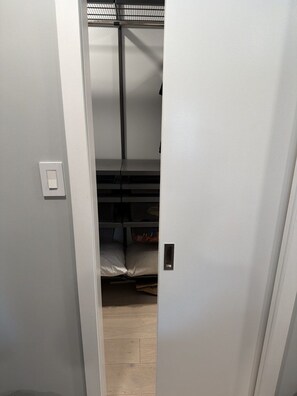 A narrow hallway leading to a room with a bunk bed, a small shelf, and a light switch on the wall.