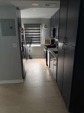 A modern kitchen with dark cabinetry, a built-in microwave, and a window with blinds.